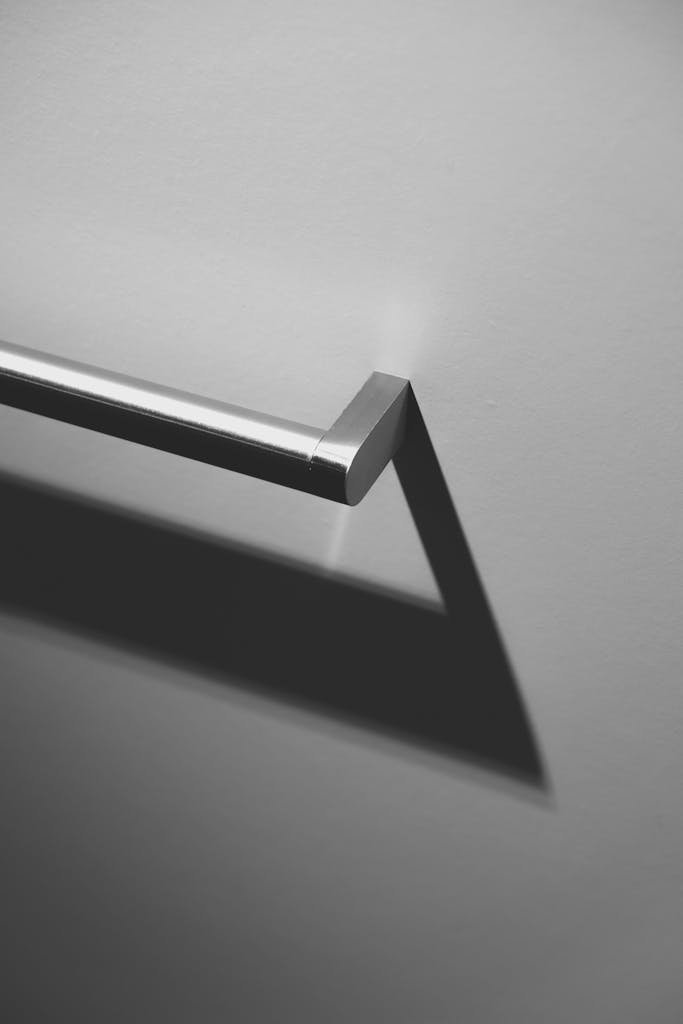 A modern stainless steel handrail casting a sharp shadow on a grey wall, showcasing minimalist design.