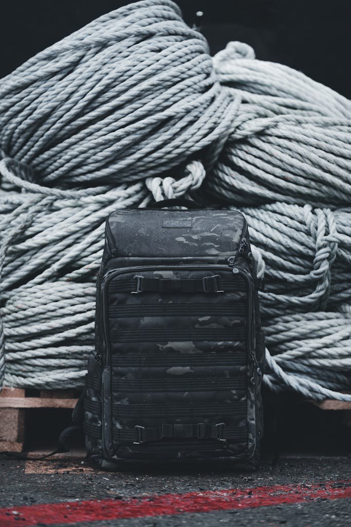 A rugged backpack placed in front of large coiled ropes, showcasing sturdy outdoor equipment.