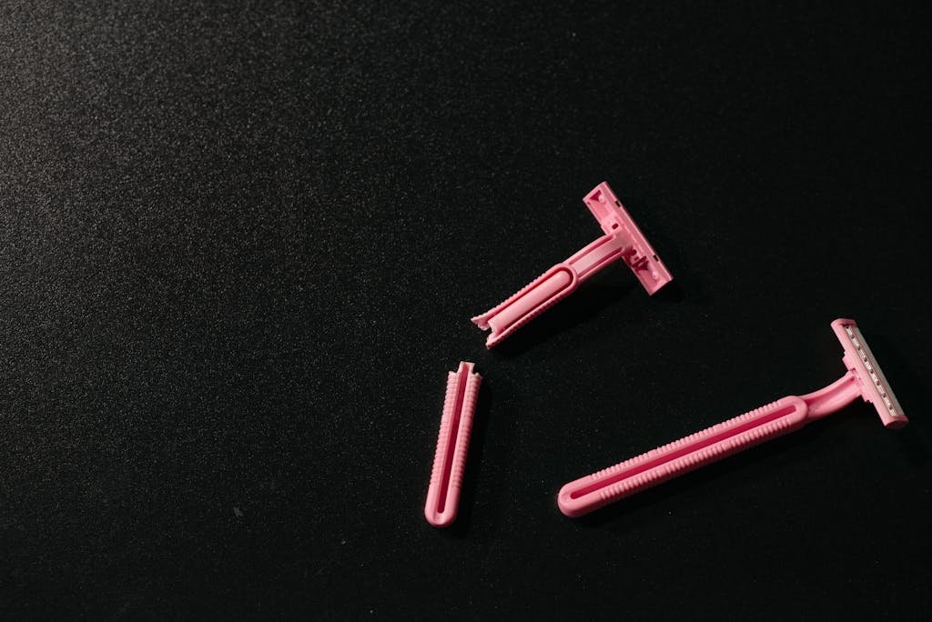 Minimalist image of intact and broken pink razors on a black background.