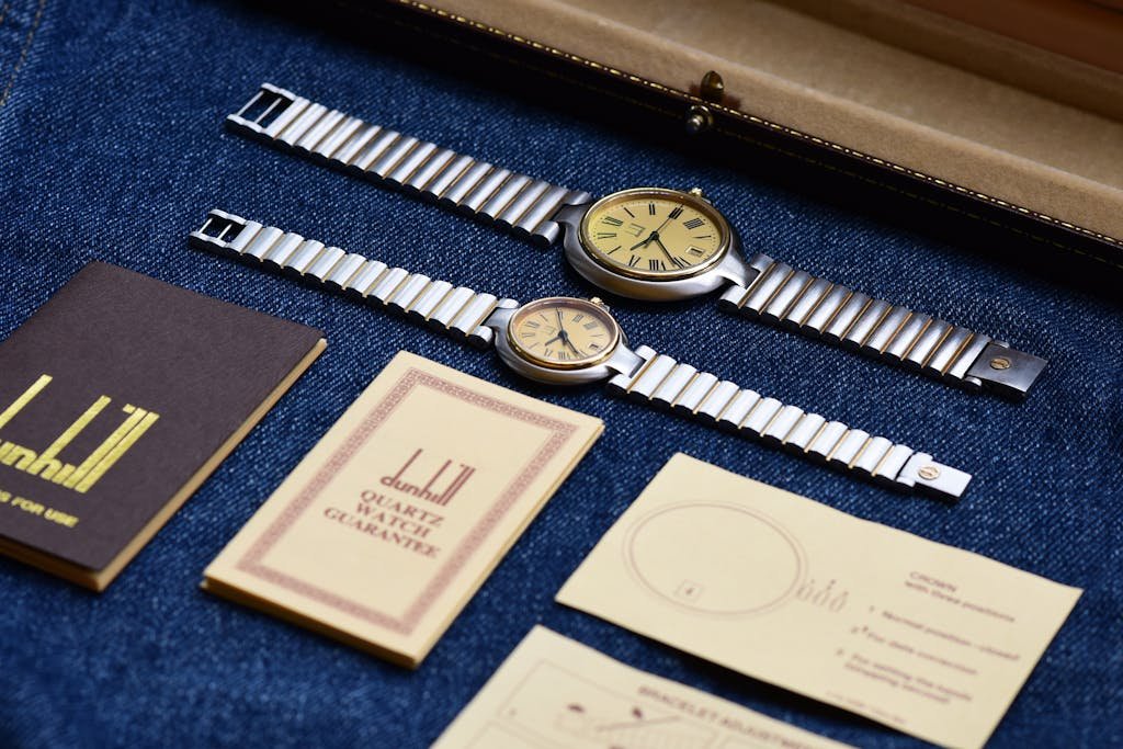 Two vintage Dunhill watches displayed on denim alongside original warranty cards.